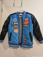 Blue quilted coat with black sleeves and Disney Cars patches hanging on a white hanger