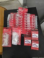 Multiple packs of white plastic Christmas light clips/hooks and boxes of metal brick hangers on black table