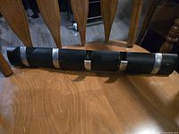 Black wall-mounted coat hanger with silver hooks laid on a wooden chair.