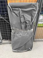 Two clothes racks folded flat and wrapped in dark grey fabric covers with white edging, taped shut for moving/storage