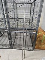 Two metal curtain rods standing vertically against a wire cage in a storage area. One rod is approximately 62 inches long, the other around 45 inches. Both rods have round decorative finials at one end. The rods have a smooth, polished silver finish.