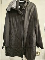 Black ladies fall coat hanging on hanger, shown front view with snap buttons and side pockets visible.
