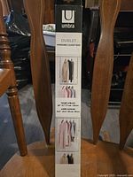 Photo of the front of the box showing Umbra Dublet Hanging Closet Rod product with adjustable height dimensions and examples of use hanging clothes.
