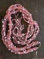 Photo of a long pink beaded necklace with white round beads resembling pearls, lying coiled on a wooden surface