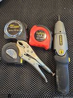 Photo of three tape measures, a Stanley rotary tool, and a locking plier on a textured black surface