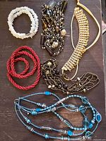 All five necklaces arranged on a dark surface showing various styles and colors.