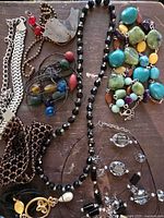 Overhead image showing 10 assorted vintage 2000s necklaces laid out on wooden surface with varied bead styles, chain types and pendants.