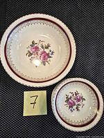Two bowls, one smaller and one larger, both featuring pink rose floral pattern with burgundy and gold rim detailing