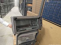 Black and Decker small countertop oven on top of a box, showing front glass door and three control knobs on the side.