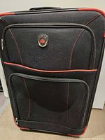 Front view of soft-sided black suitcase with red trim, two zippered compartments, and Canada emblem.