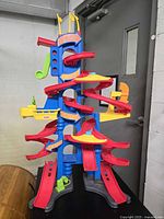 Front and angled view of the Fisher-Price toy garage showing multiple red spiral ramps around a blue plastic tower with yellow and orange attachments on a black base.