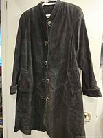 Full front view of black suede trench coat hanging on a white hanger, showcasing button closure and patch pockets.