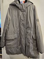 Front view of a gray ladies winter coat in size 2X showing hooded parka style, zipper with button closures, and two zippered front pockets with flaps.