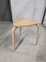 Wooden stool with triangular seat and three curved legs; clear view of legs and underside of seat showing wood grain and structure.