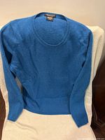 Front view of the blue cashmere sweater laid flat showing full body and sleeves.