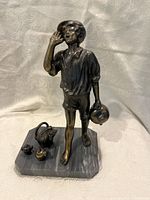 Front view of bronze statue showing boy holding jug with raised hand, mounted on marble base with small bronze items nearby.