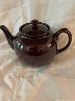 Full side view of the glossy brown Brown Betty teapot on a cream textured fabric background.