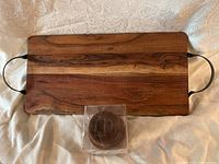 Full view of rectangular acacia charcuterie board with metal handles and 3 acacia mini bowls still in original packaging placed in front.