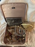 The open Lancôme soft bag with glittery black clutch purse, gold rhinestone clutch purse, and assorted costume jewelry piled inside.