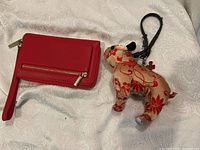 Both red leather wallet and fabric dog-shaped keychain on white patterned fabric