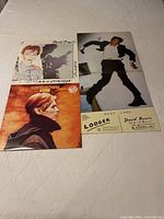 Photo of three David Bowie vinyl albums: Scary Monsters, Low, and a Lodger postcard laid on a white quilt.