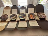 Five Norman Rockwell collectible plates displayed in their open boxes with certificates visible.