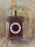 Front-facing view of clear glass bottle with round white label reading “Guerlain Paris Insolence” and pink-purple liquid inside