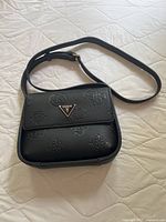 Front side of the black Guess purse showing embossed logos and gold-tone logo plaque on front flap.