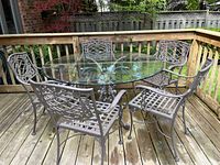 Full set of round glass-topped table with five wrought iron chairs on wooden deck