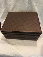 Top and front view of large brown faux leather jewelry box with textured pattern and two compartments.