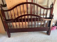 Full view of queen size bed frame with curved headboard and footboard with spindles and finials on posts, cherry wood finish.