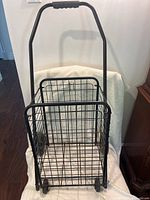 Front view of black metal folding cart showing wireframe basket and handle with foam grip