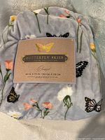 Photo of folded plush polyester blanket with original label showing brand Butterfly Skies Home Collection, dimensions 60 x 70 inches, and made in China.