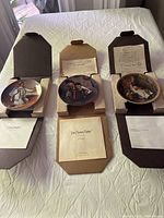 Three Norman Rockwell collector plates with open original packaging and certificates of authenticity visible
