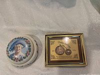 Porcelain commemorative dish with Queen Mother portrait and framed Penny Farthing souvenir shown side by side on white textured fabric surface.