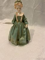 Front view of Royal Worcester porcelain figurine of woman in green dress with bonnet and purse