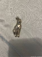 Front view of sterling silver cat pendant on textured fabric background, showing cat posture and loop attachment.