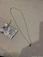 Full view of the sterling silver necklace laid out flat next to the metallic pouch on a textured fabric surface.