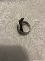 Sterling silver ring with twisted band set with multicolor jewels on white patterned fabric.