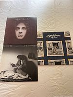Three vinyl albums laid out on a quilted surface: Billy Joel's The Stranger, Loggins & Messina's So Fine, and an unshown third album.