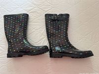Side view of the pair of black rubber boots with colorful polka dots on light background, shows height and buckle detail.