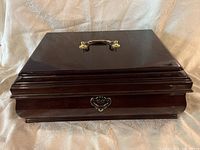 Closed dark brown wooden jewelry box showing overall shape with brass handle and keyhole plate on front.