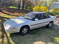 Front-side view of white two-door coupe with pop-up headlights and black stripe