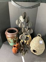 Full lot overview showing stoneware pot, paired terracotta bird houses, woven bee skeps, cast iron snail candle holder, and hanging wind chimes.