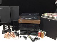 Full view of the audio equipment lot showing turntable on top, amplifier and CD player below, two speakers on stands, AV cables coiled, several vinyl albums stacked, and other accessories.