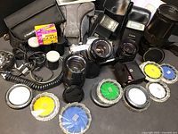 Complete lot showing Canon AE-1 camera mounted with 50mm lens, additional lenses, two flash units, multiple filters, cables, film, and camera case.