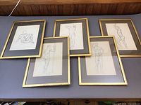 Five framed pencil drawings of male nude studies arranged on a wooden surface, each framed in gold wood with grey/blue mats.