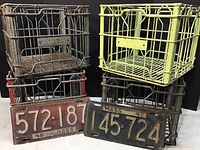 Four metal Hood dairy milk bottle crates stacked with two antique Massachusetts license plates in front showing plates dated 1947 and 1948.