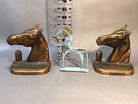 Front view of the brass horse head bookends with the smaller Etruscan style horse figurine placed in the middle, ruler showing approximately 5.5 inches tall.
