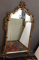 Full front view showing the large rectangular mirror with ornate gilded gold floral frame and small inlaid mirrors in the frame